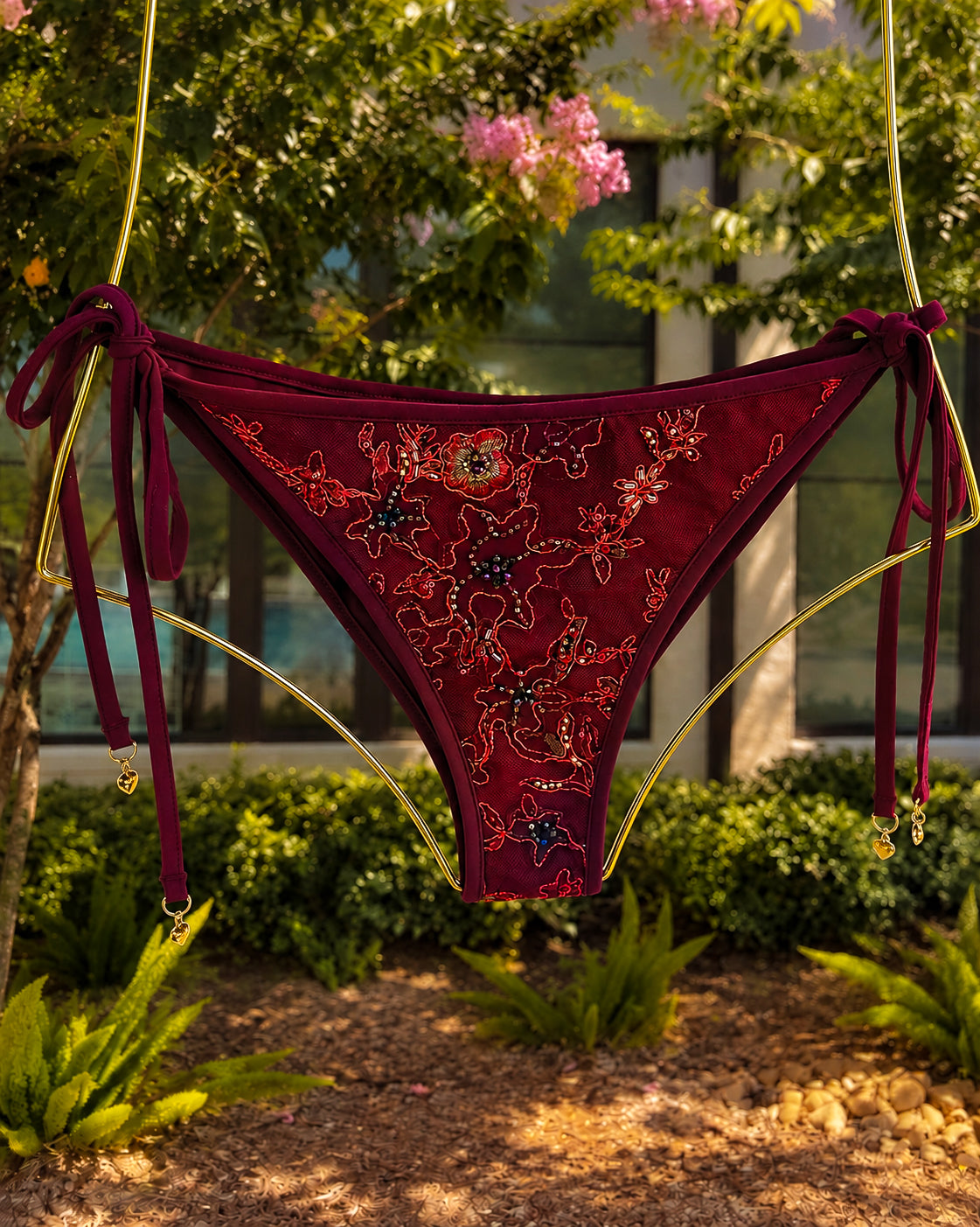 The Evangeline Crimson bikini, hanging from a gold metal frame in an outdoor garden setting.