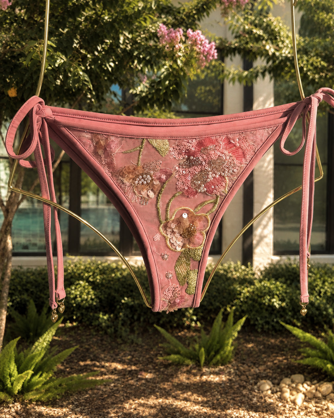 The Evangeline Blush bikini, hanging from a gold metal frame in an outdoor garden setting.