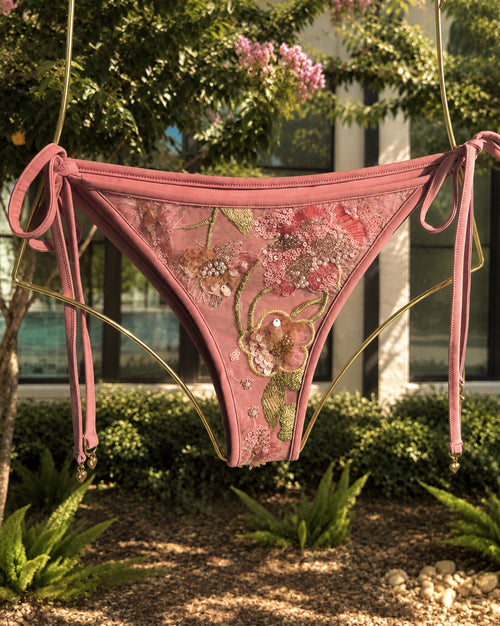 The Evangeline Blush bikini, hanging from a gold metal frame in an outdoor garden setting.